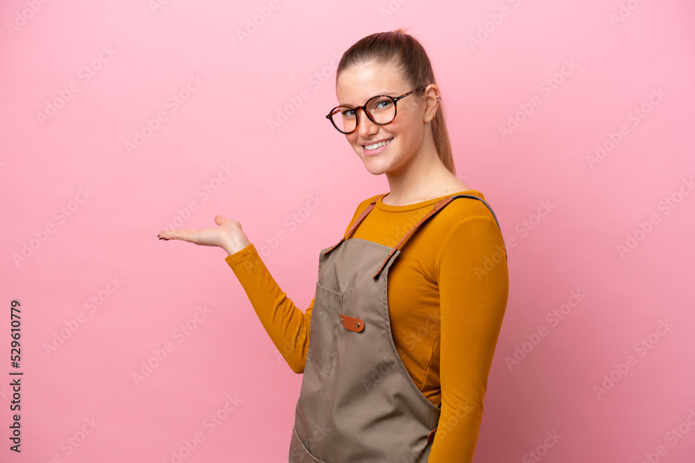 Woman with apron isolated on pink background extending hands to the side for inviting to come