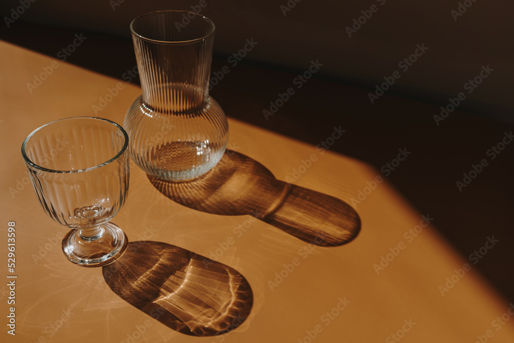 Aesthetic luxury bohemian concept. Crystal glass and vase on warm tan orange background with sunlight shadows