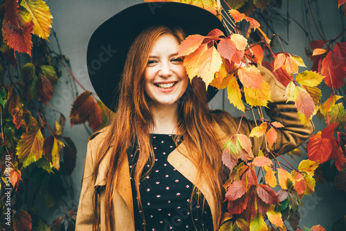 Pretty woman in hats with autumn leaves. The girl closing face the autumn leaf and having hun in the park. Concept of good mood at the autumn time. photo