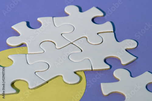 Close-up on jigsaw puzzle pieces, blank white paper jigsaw puzzle elements linked together and separate. Closeup shot on yellow and purple paper. Abstract background metaphor on teamwork challenge.