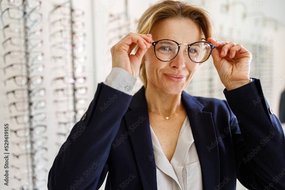 Smiling Middle-aged woman chooses glasses in an optics store Smiling Middle-aged woman chooses glasses in an optics store