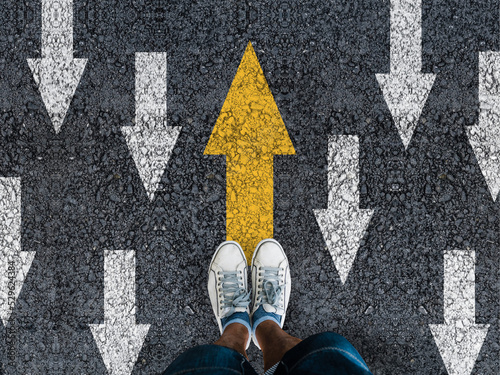 man sneakers on asphalt and opposing direction arrows on asphalt ground, personal perspective footsie concept for finding your own way
