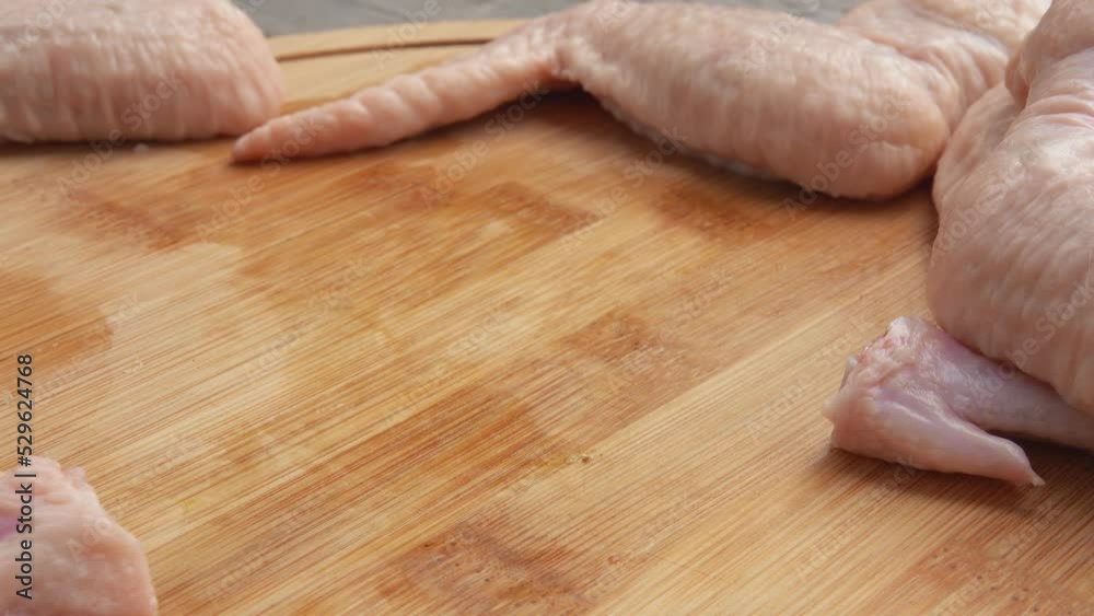 Close-up of male hands cutting chicken wings with a knife on the wooden board Close-up of male hands cutting chicken wings with a knife on the wooden board