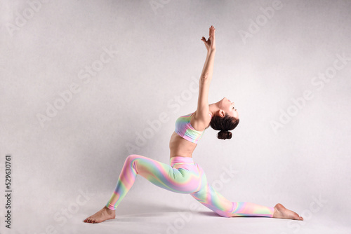 A beautiful slender gymnast in a stretch in a tracksuit does sports or yoga in the studio flexibly bending her torso and body in the studio on a white background