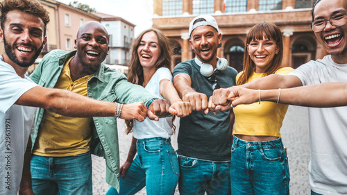 Multiracial group of young people making fist bump as symbol of unity, community and solidarity - Happy friends portrait standing outdoors - Teamwork join hands and support together