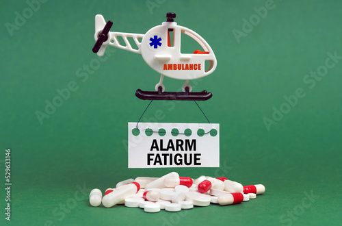 On a green surface, an ambulance helicopter, pills and a white sign with the inscription - ALARM FATIGUE photo