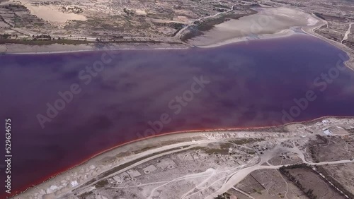 Aerial footage of pink lake with stacks of salt and roads made of salt along its shore, clouds reflecting on the lake, Retba lake, Dakar, Senegal, panning along the lake. photo