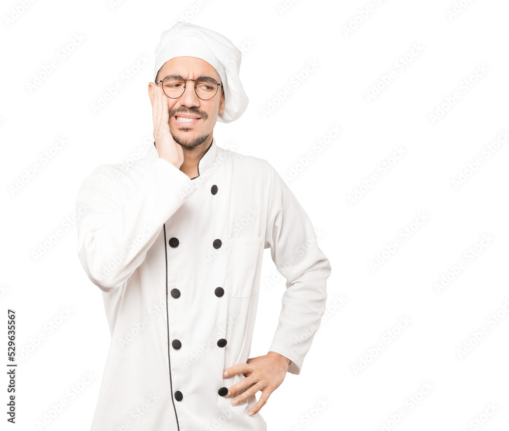 Concerned young chef with a toothache gesture Concerned young chef with a toothache gesture