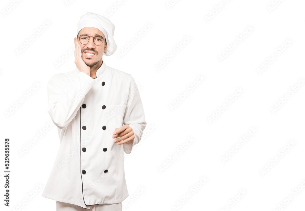 Concerned young chef with a toothache gesture Concerned young chef with a toothache gesture