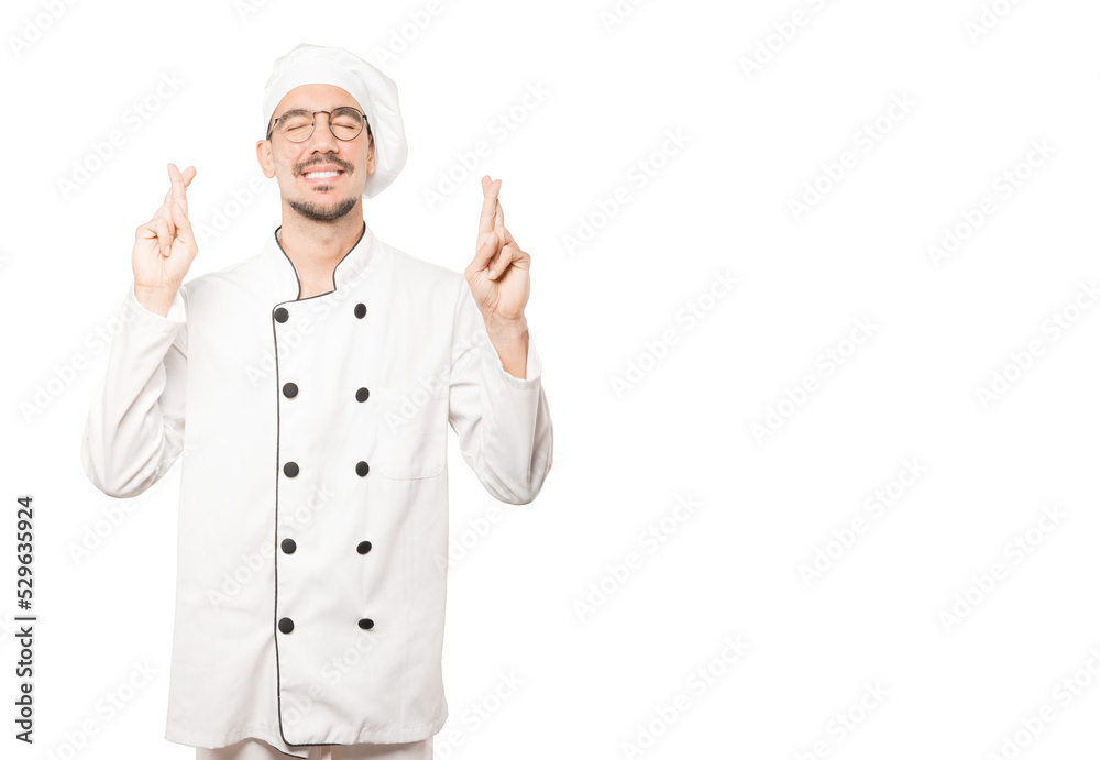 Happy young chef doing a crossed fingers gesture Happy young chef doing a crossed fingers gesture