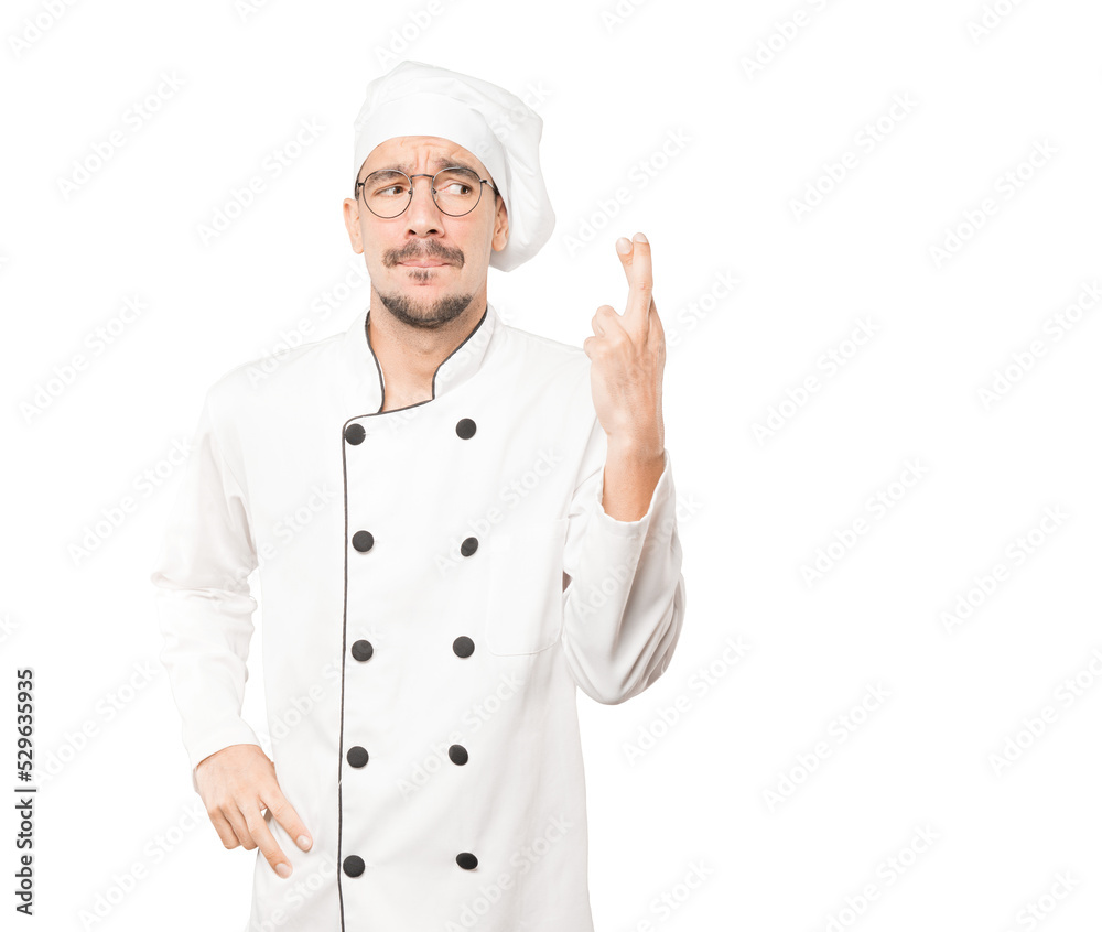 Concerned young chef doing a crossed fingers gesture Concerned young chef doing a crossed fingers gesture