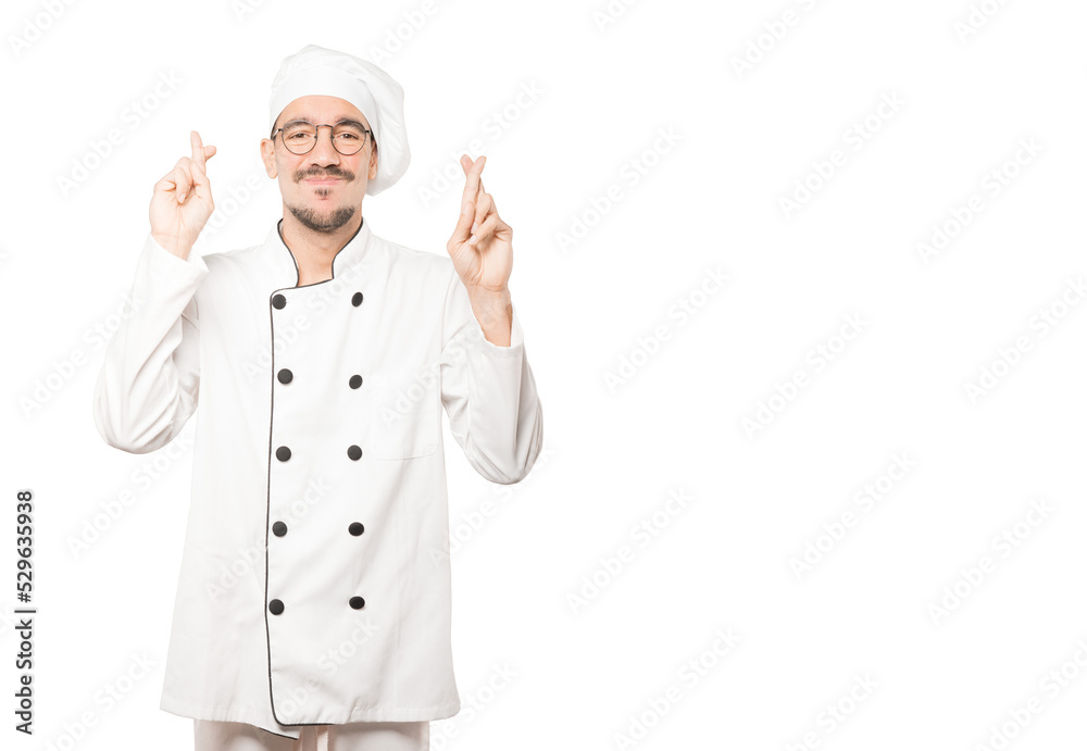 Concerned young chef doing a crossed fingers gesture Concerned young chef doing a crossed fingers gesture
