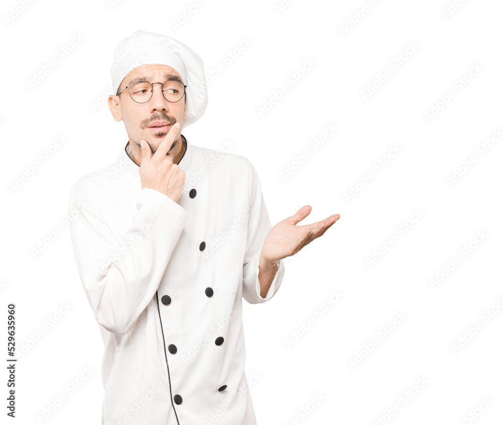 Concentrated young chef making a gesture of distrust Concentrated young chef making a gesture of distrust