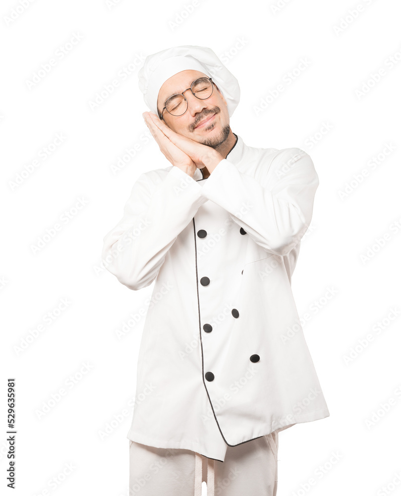 Relaxed young chef making a gesture of sleep Relaxed young chef making a gesture of sleep