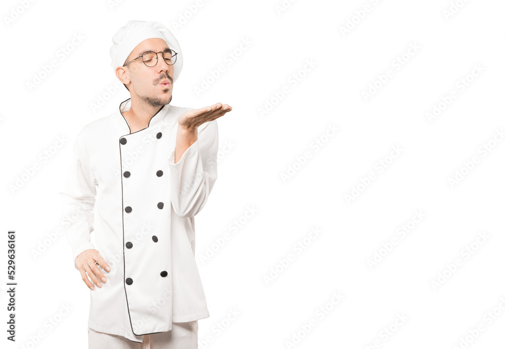 Friendly young chef making a gesture of sending a kiss with his hand Friendly young chef making a gesture of sending a kiss with his hand