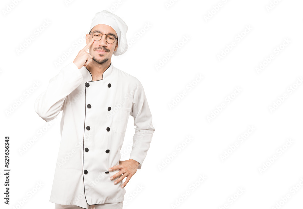 Hesitant young chef making a gesture of being careful with his hand pointing at his eye