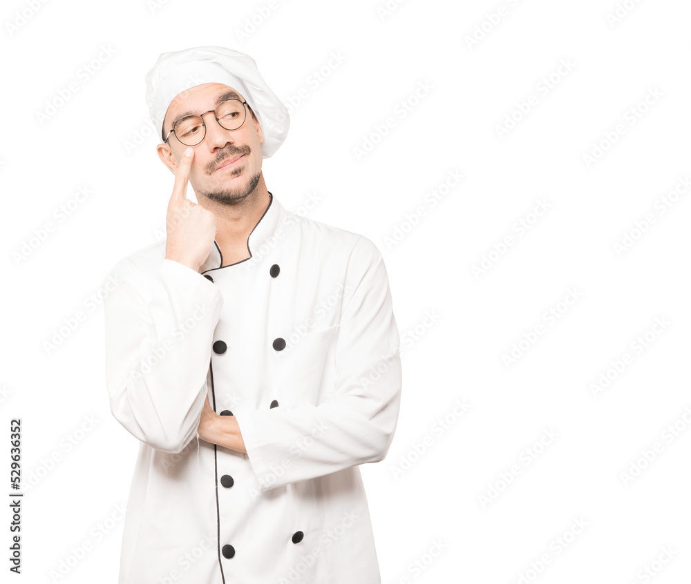 Hesitant young chef making a gesture of being careful with his hand pointing at his eye Hesitant young chef making a gesture of being careful with his hand pointing at his eye