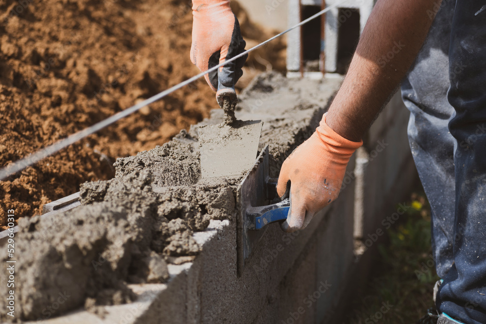 Obraz premium Bricklayer in glove spreading concrete to build a wall on construction site