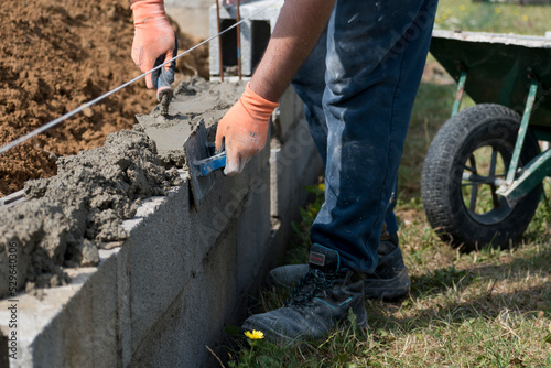 Bricklayer in glove spreading concrete to build a wall on construction site