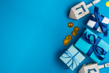 Dreidel, dreidle or dreidl with blue lettering on bright background. Gift box, spinning top, Jewish holiday of Hanukkah, Jewish teetotum, gold coins