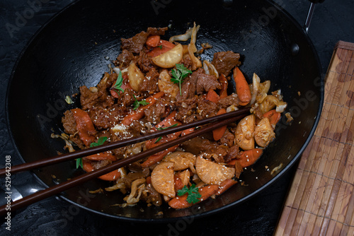 Seitan, daicon and carrot stir fry in wok on black table photo