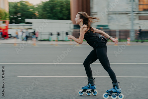 Active leisure concept. Full length shot of young slim woman rollerblades along asphalt on street enjoys speed spends free time on favorite hobby poses outdoors breathes fresh air. Rollerskating