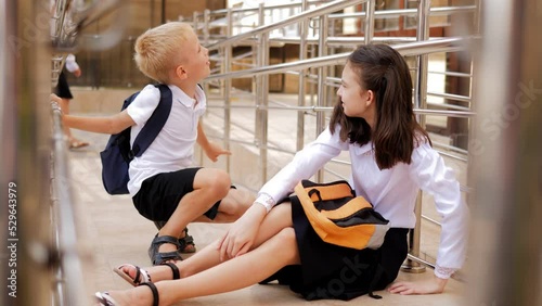 A schoolboy boy in a school uniform sticks to a schoolgirl girl sitting on the floor. Bullying in elementary school. photo