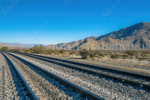 Windmills on a wind park along a railroad track with clear blue sky view