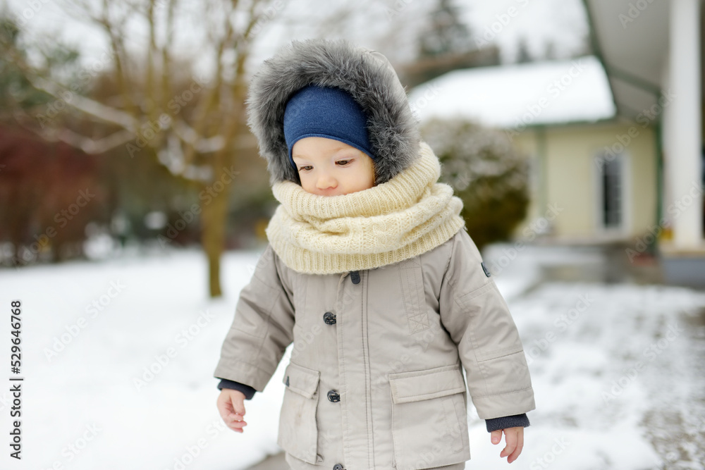 Obraz premium Adorable toddler boy having fun in a backyard on snowy winter day. Cute child wearing warm clothes playing in a snow.