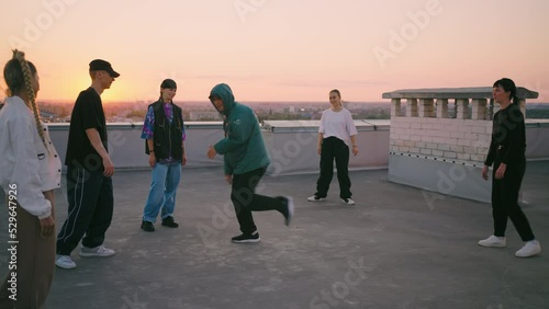cool breakdancer boy is dancing on roof, young guy in trendy hoody is breaking on floor, friends dance party photo