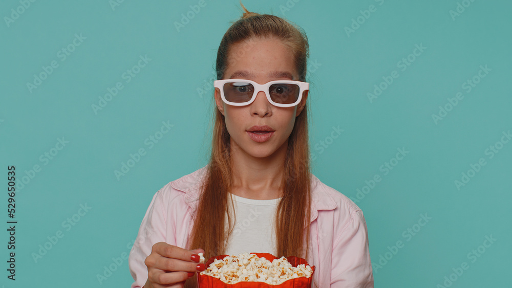 Excited teenager girl eating popcorn and watching interesting tv serial, sport game film, online social media movie content online. Student child kid on blue background enjoying domestic entertainment