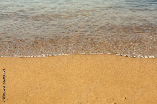 Background with golden sand on the coast of the island of Crete. Abstract surface with sand and clear sea water for text.