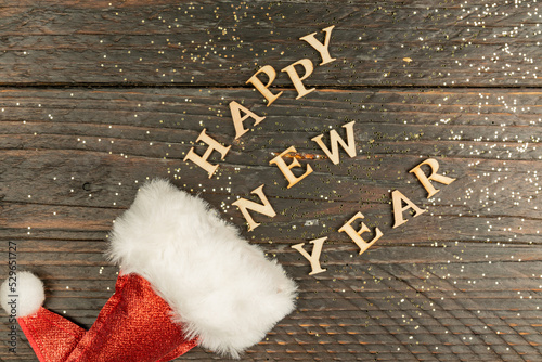 Red santa hat and scattered out wooden letters on wooden background, festive greeting card for winter holidays.