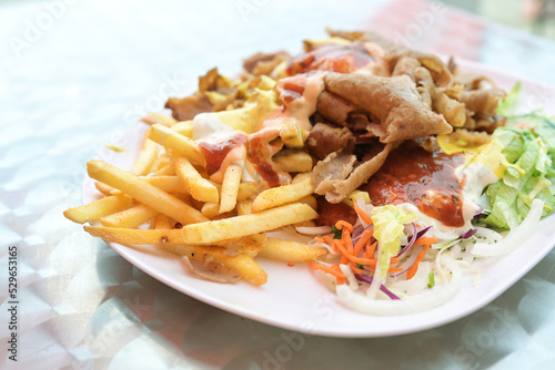 Doner kebab on a plate with French fries, salad and various sauces on a plate, popular fast food from Turkish cuisine, copy space, selected focus