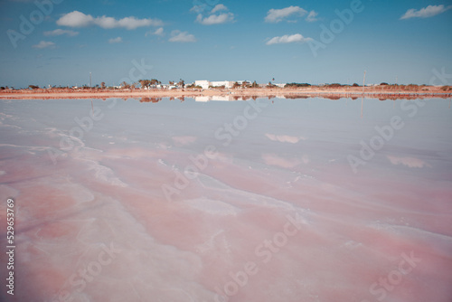 Pink lake with clouds reflection, Atlit, Israel. Salt production facilities saline evaporation in salty pond. Dunaliella salina impart red, pink water in mineral lake with dry cristallized salty coast photo