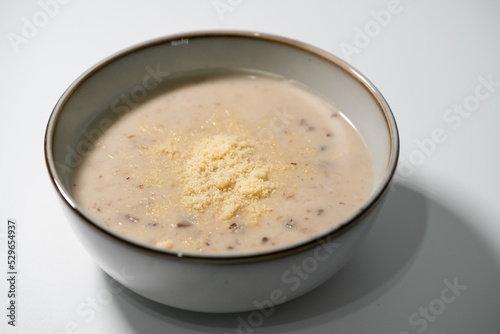 Homemade mushroom soup with parmeson cheese topping in stoneware bowl isolated on white background.