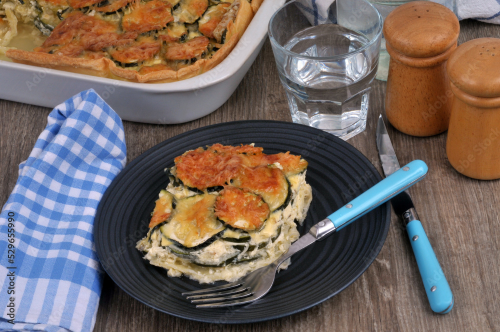 Assiette de gratin de courgettes servie avec un verre d'eau Assiette de gratin de courgettes servie avec un verre d'eau