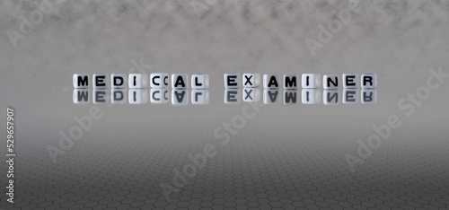 medical examiner word or concept represented by black and white letter cubes on a grey horizon background stretching to infinity photo