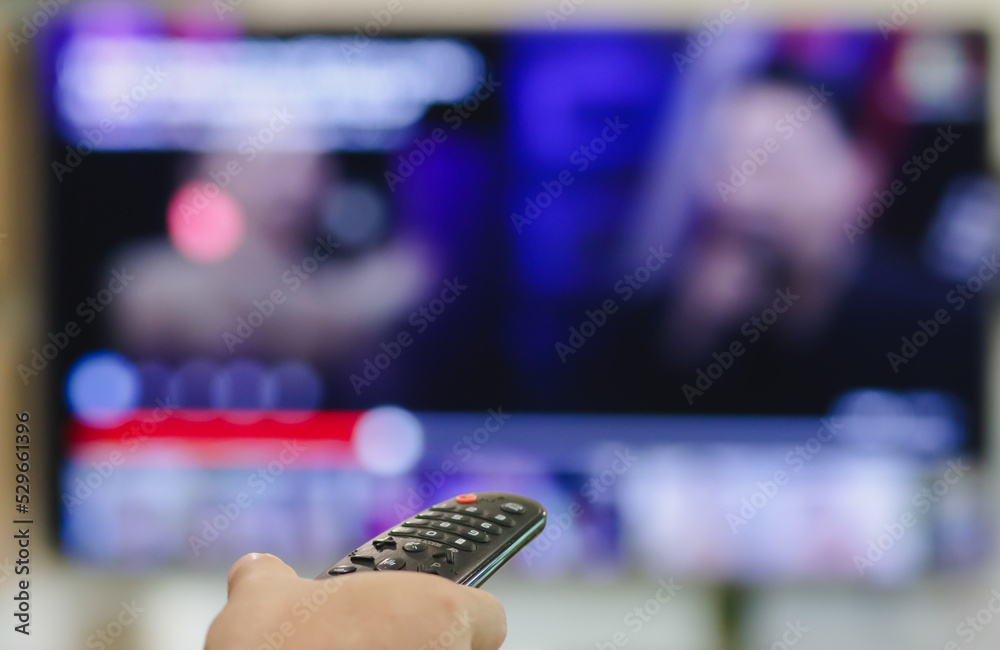 Close-up of hand with the remote control television and presses the button. Television remote control changes channels thumb on the blue TV screen.