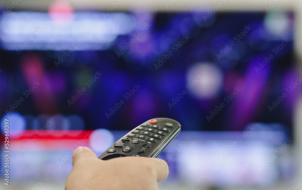 Close-up of hand with the remote control television and presses the button. Television remote control changes channels thumb on the blue TV screen.