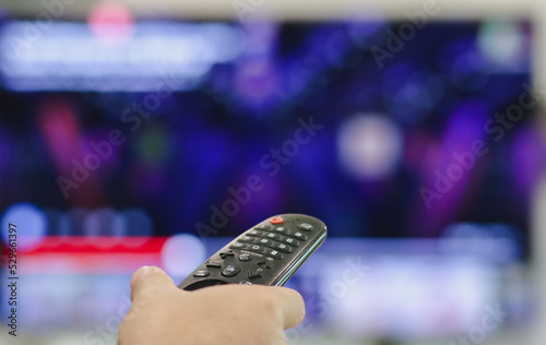 Obraz na płótnie Close-up of hand with the remote control television and presses the button. Television remote control changes channels thumb on the blue TV screen. w salonie