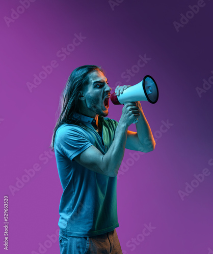 Young handsome guy emotionally screams into a bullhorn. colored neon light studio 