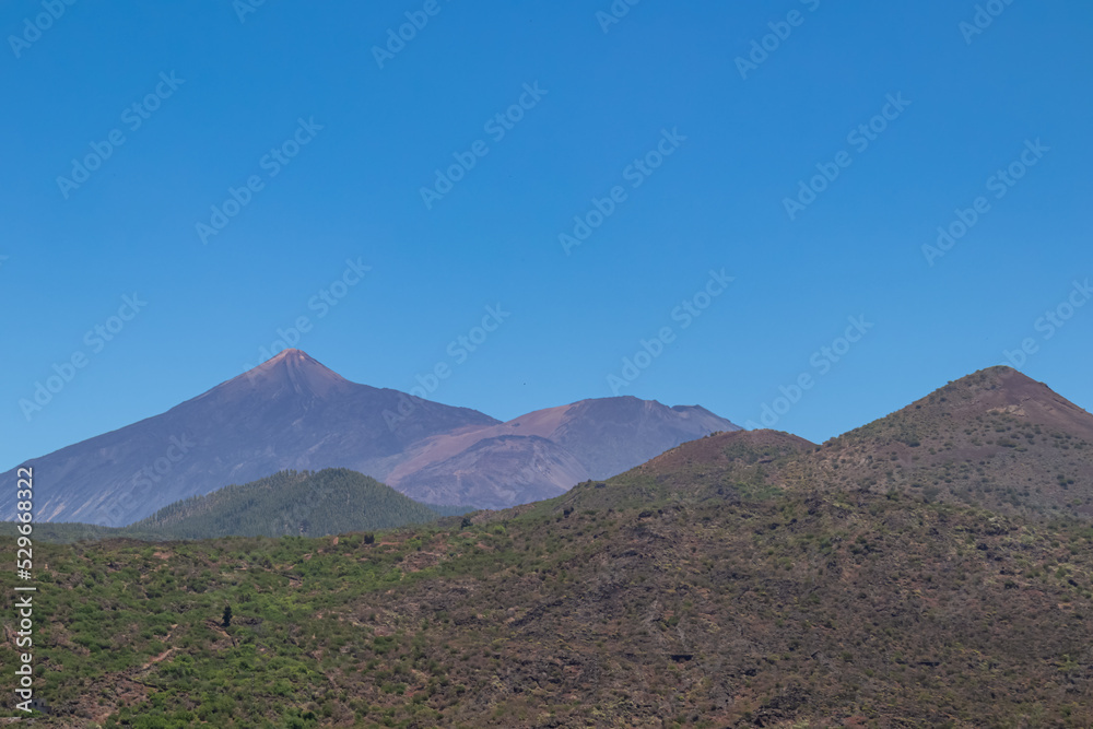 Panoramic view on volcano Pico del Teide seen from Pico Verde, Teno mountain range, Tenerife, Canary Islands, Spain, Europe. Lush green vegetation on the hills in foreground. Hiking in Masca village