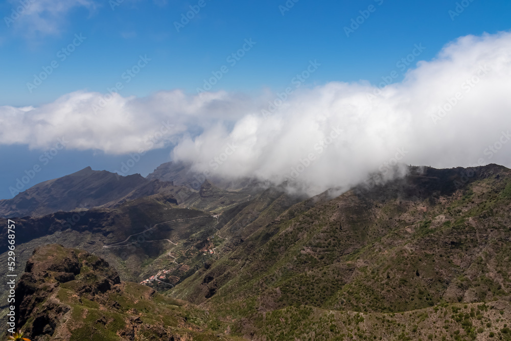 Panoramic view on the Teno mountain massif seen from summit Pico Verde, Tenerife, Canary Islands, Spain, Europe. Hiking trail between Masca and Santiago. Clouds over lush green hills. Tropical climate