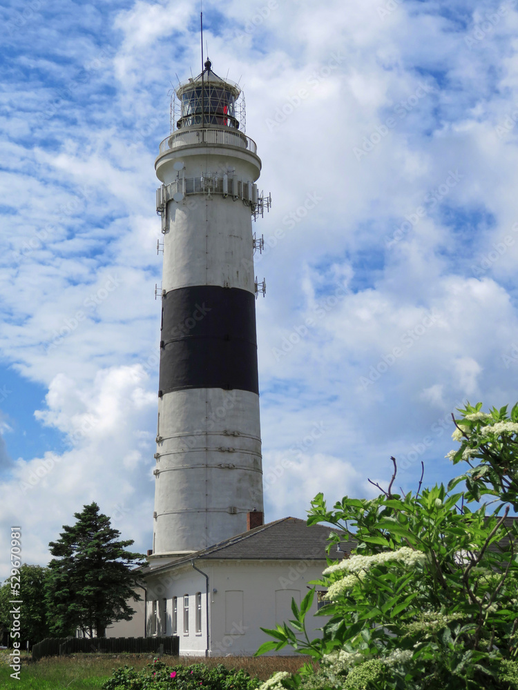 White lighthouse with a black stripe behind a meadow and houses in front of a cloudy sky on Sylt, Germany