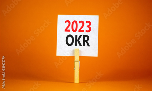 OKR objectives and key results symbol. White paper, words OKR 2023 clip on wooden clothespin. Beautiful orange table orange background. Business OKR 2023 objectives and key results concept. Copy space