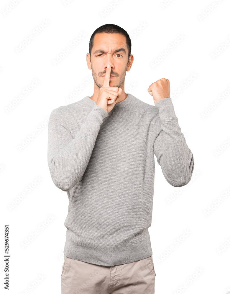 Serious young man asking for silence gesturing with his finger Serious young man asking for silence gesturing with his finger