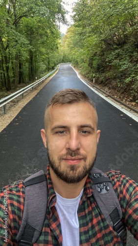 A guy takes a selfie on a scenic forest road.
