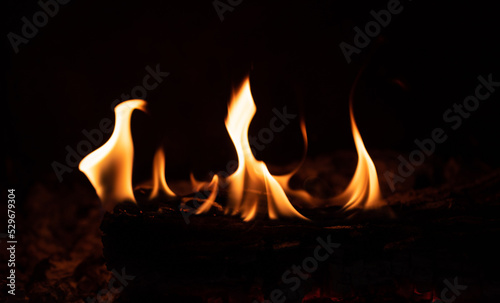 Flame in the fireplace, yellow tongues of fire. Black background. Firewood burning. Heating the house with a fireplace.
