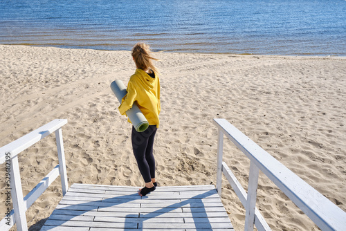 A sporty girl with an exercise mat is preparing for yoga on the sea or ocean. Fitness yoga workout outdoors near the water. Wellness and sport concept